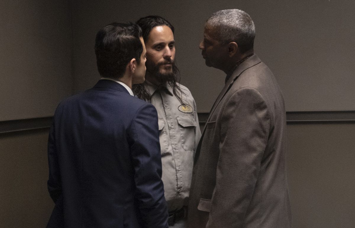 In an interrogation room, Rami Malek in a blue suit and Denzel Washington in a brown suit stand up in the face of Jared Leto who looks like Charles Manson in The Little Things