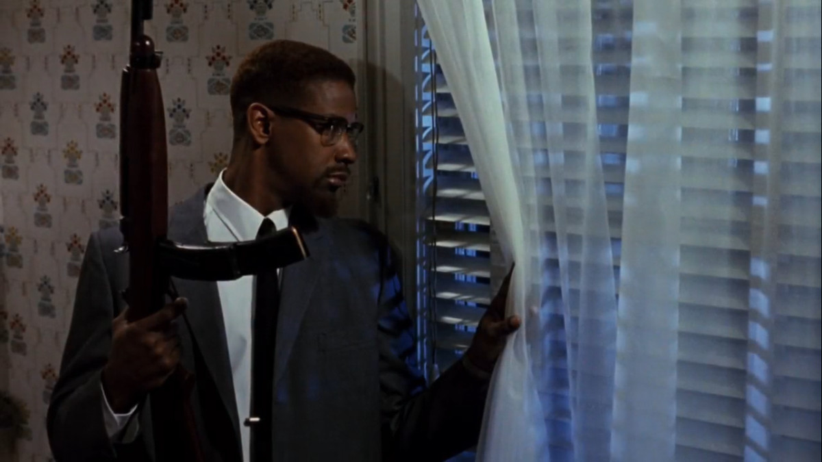 Denzel Washington peering out the window with a rifle as Malcolm X in Malcom X