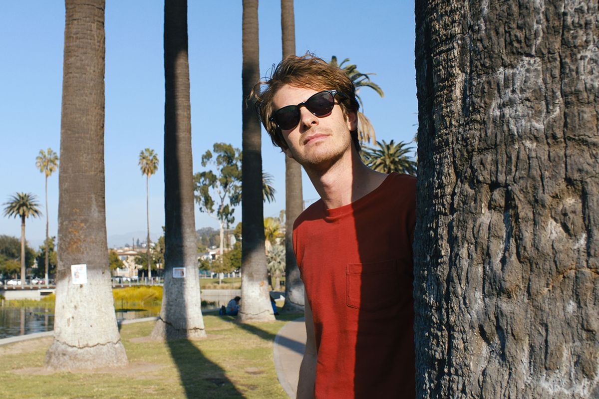 andrew garfield peeks from behind a palm tree with his sunglasses on