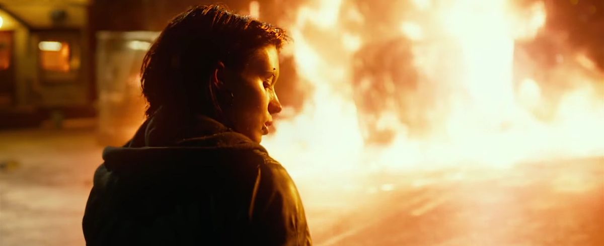 Rooney Mara as Lisbeth Salander stands in the foreground while a car burns in the background in The Girl With the Dragon Tattoo