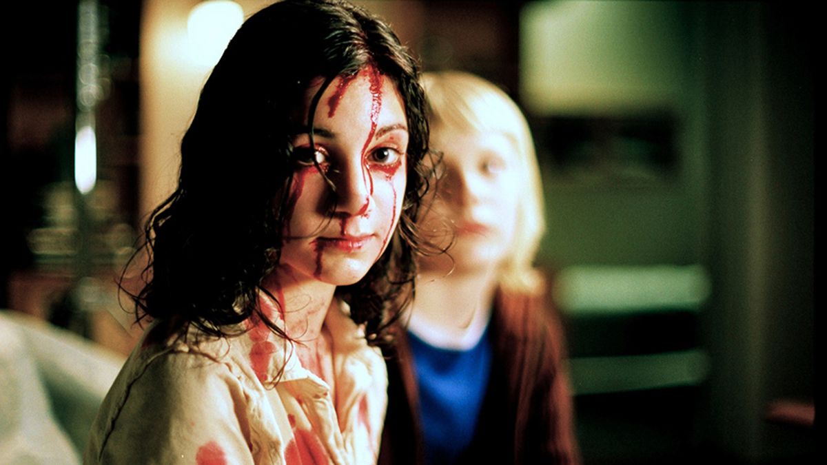 Lina Leandersson, a dark-haired little girl with wide eyes, sits covered in blood in Let the Right One In.