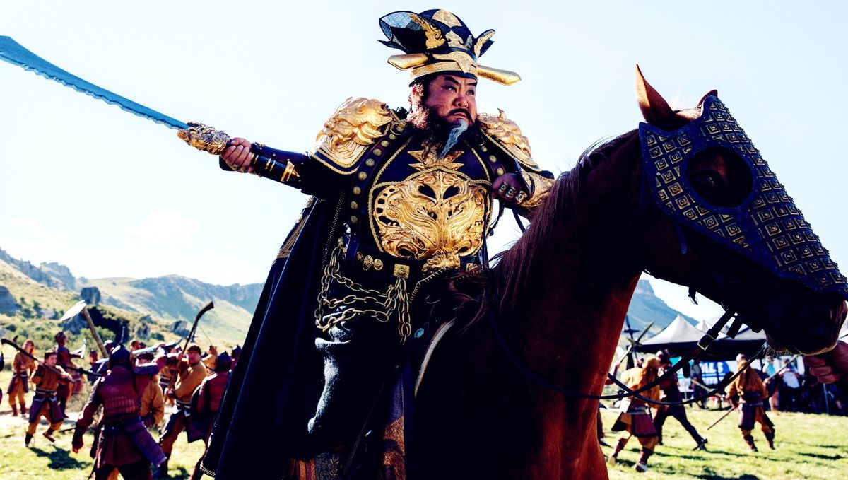 A bearded warrior in gilt armor on an armored horse charges into battle in Dynasty Warriors