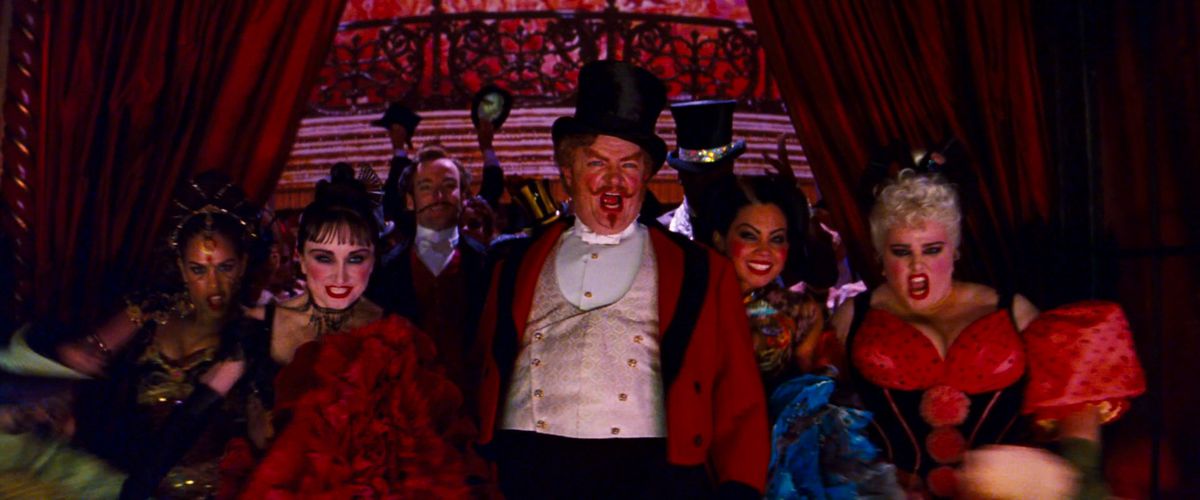 Jim Broadbent leads a chorus of chorus girls through the red curtains in Moulin Rouge