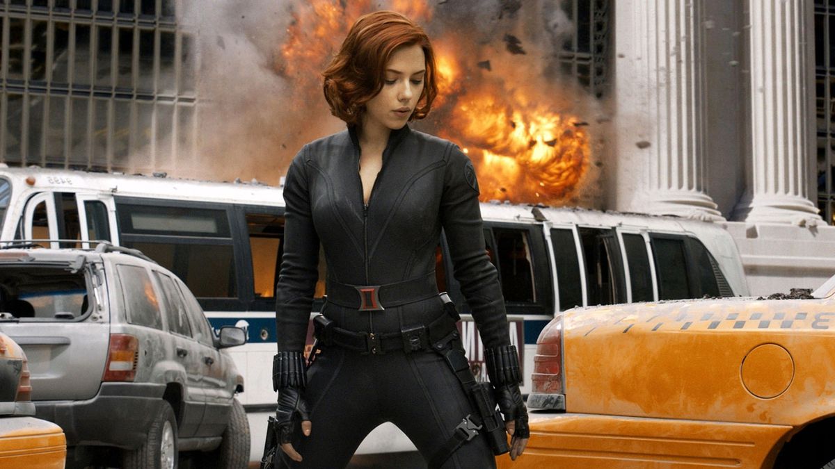 Black Widow standing in New York City with an explosion above a bus behind her