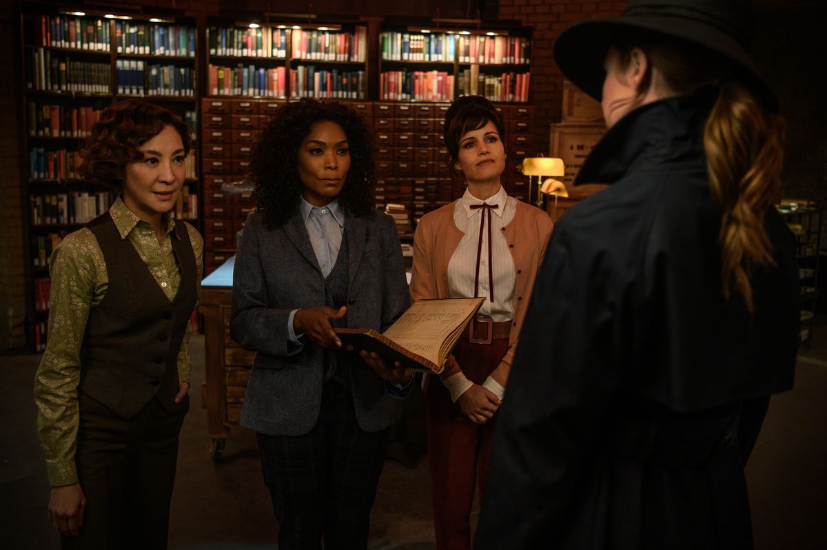 Karen Gillan, seen from behind and wearing a hat and trenchcoat, faces a panel of weaponeers&nbsp;—Michelle Yeoh, Angela Bassett, and Carla Gugino —&nbsp;in Gunpowder Milkshake