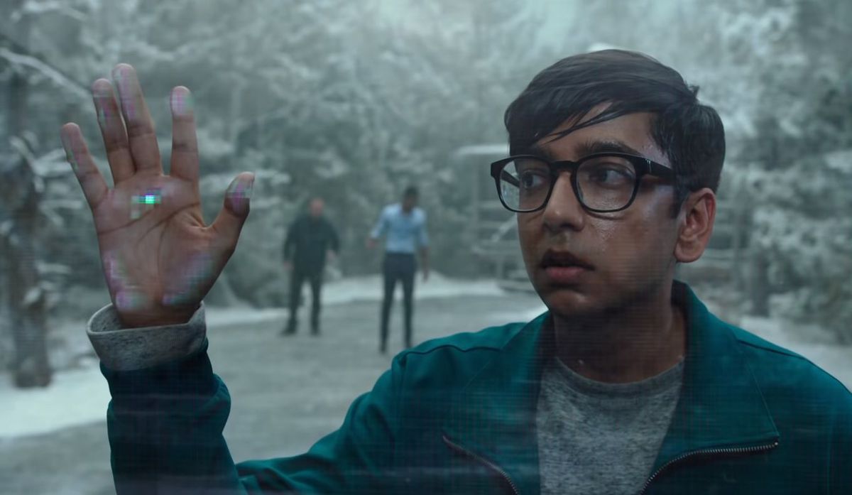 A young man with glasses standing on what appears to be a snowy road outside puts his hand up to the fourth wall and encounters a glitchy force field in 2019’s Escape Room