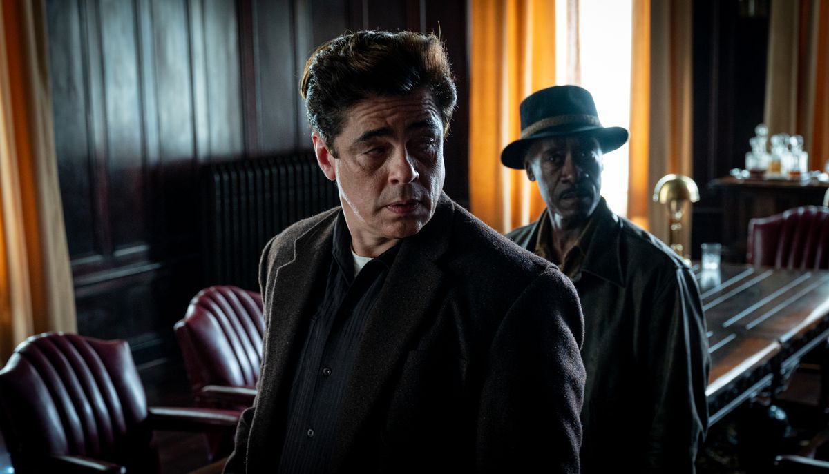 Benicio del Toro and Don Cheadle stand in a dark room with bright curtains behind them in No Sudden Move
