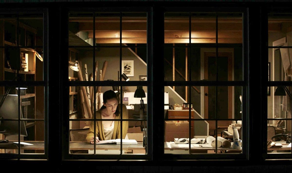 Rebecca Hall in The Night House, seen in the dark through a series of windows, from outside her house
