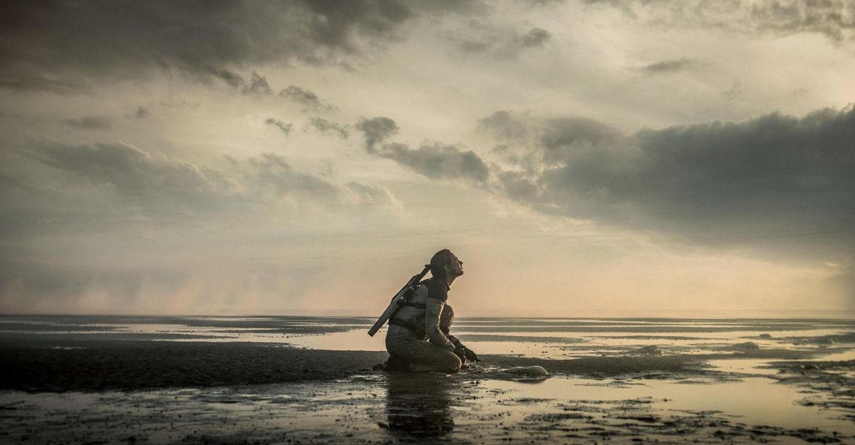 A lone woman with a rifle kneels on a placid, alien-looking shore