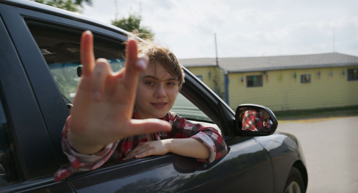 Emilia Jones leans out of a car to sign at the camera in CODA