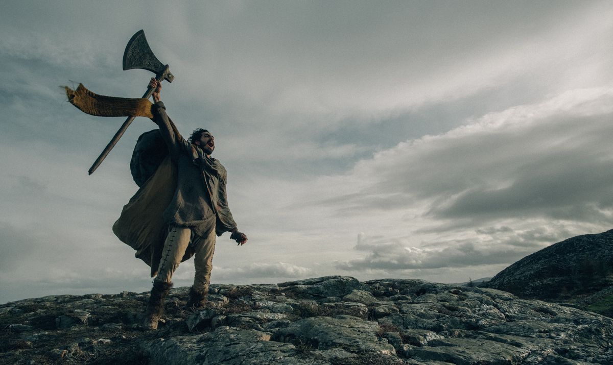 Dev Patel as Sir Gawain lifting an axe and shouting atop a mountain in The Green Knight