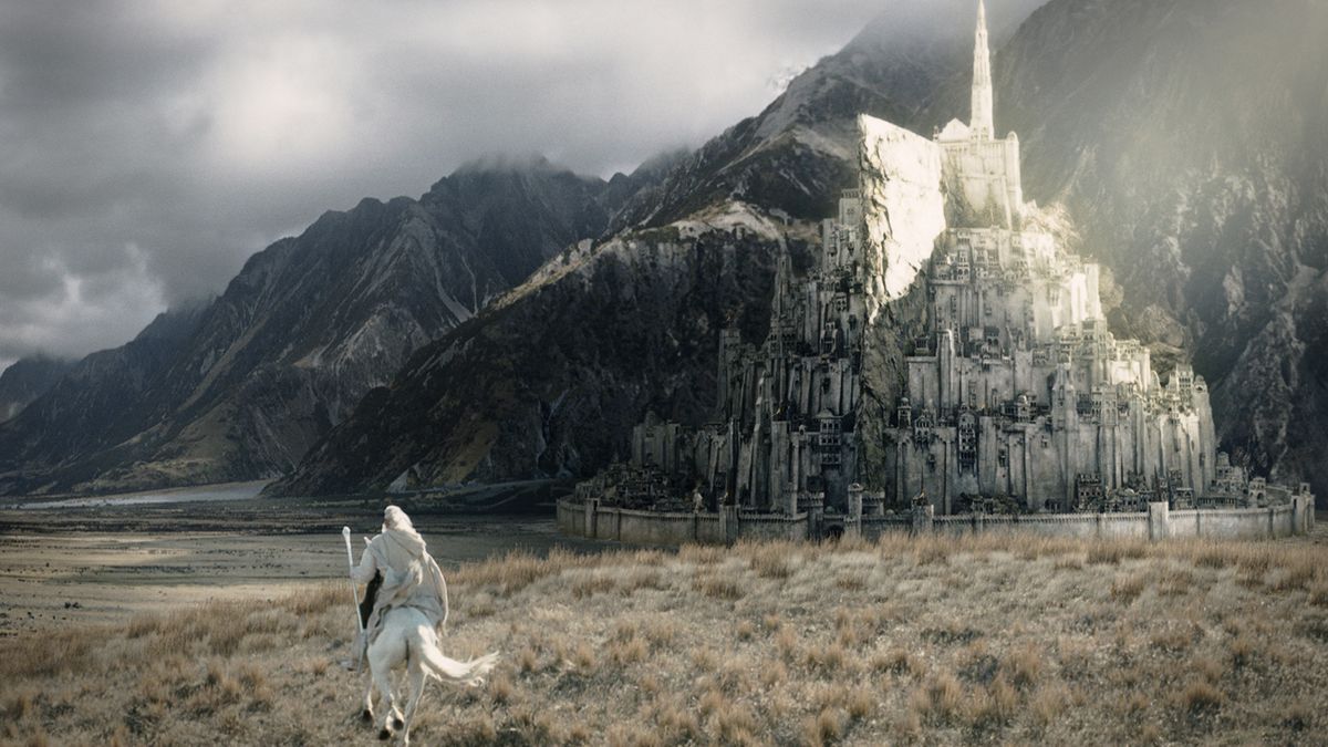 Gandalf (McKellen), clad in white and riding a white horse, approaches a city built out of the side of a mountain.