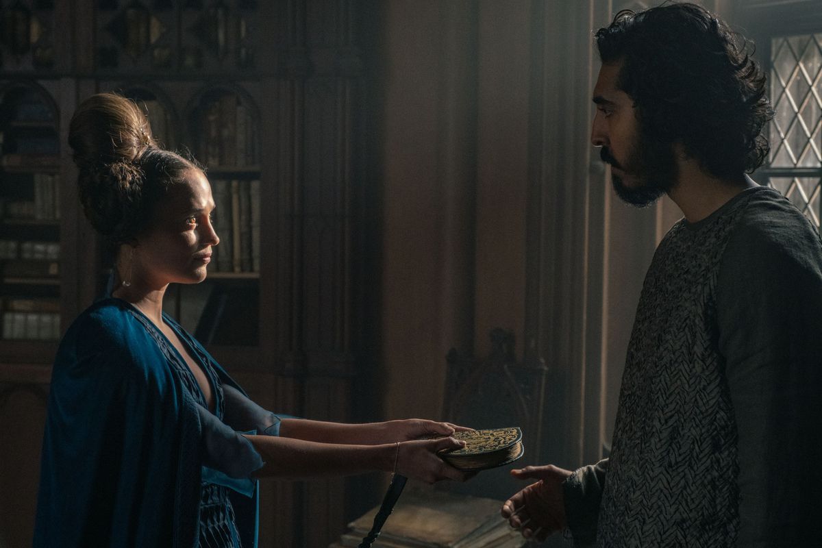 Alicia Vikander hands Dev Patel a book of love poems in The Green Knight