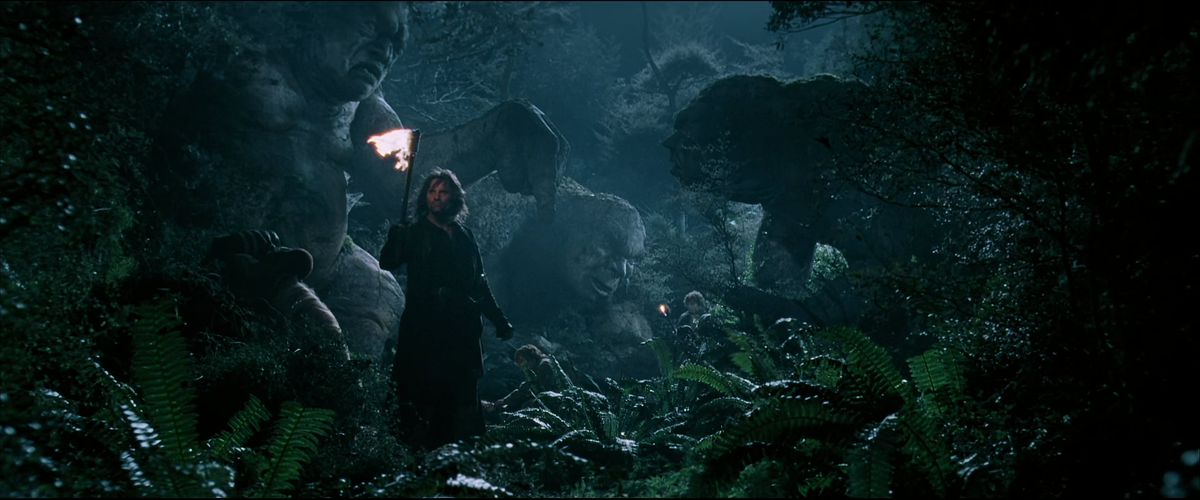 Aragorn holds a torch in front of three trolls that have been frozen in stone in The Fellowship of the Ring. 