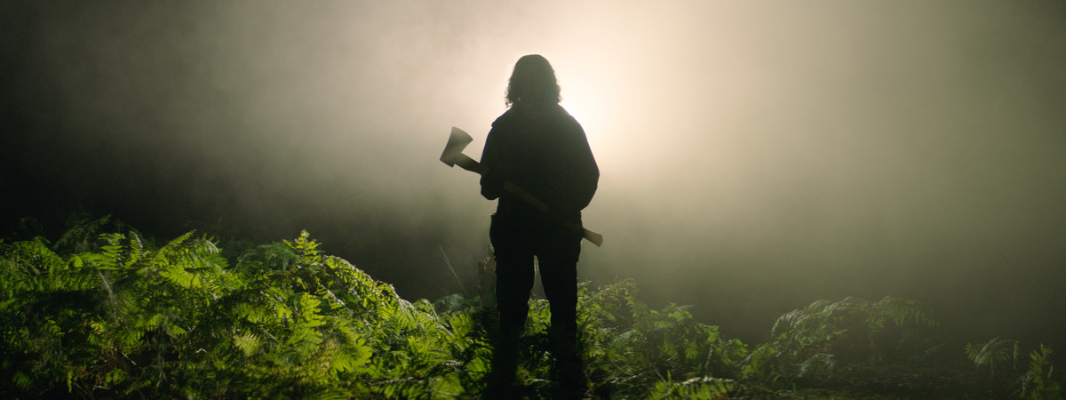 A silhouetted figure in the forest, clutching an axe, in In the Earth