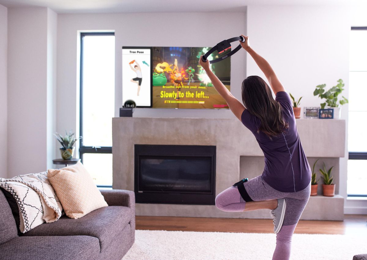 a woman in exercise gear holds a yoga pose with the Ring-Con while playing Nintendo’s Ring Fit Adventure